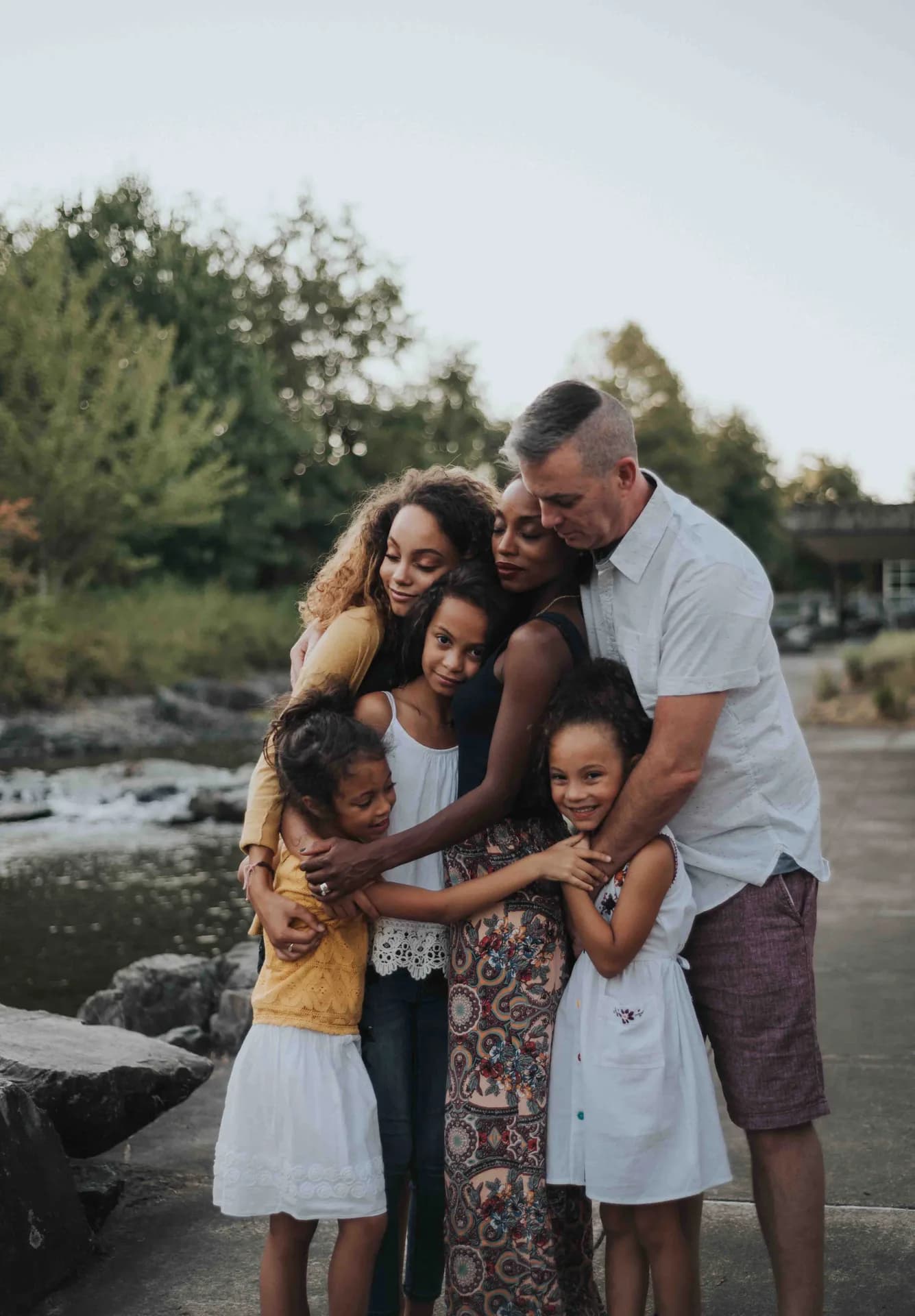 A family sharing a group hug beside a rocky pond.